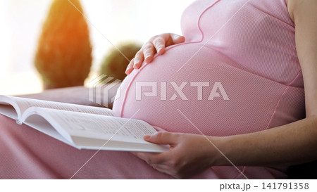 Pregnant woman reading book and touching belly with caring hand Pregnant woman reading book and touching belly with caring hand 141791358