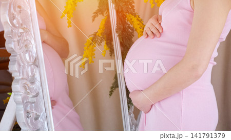 Pregnant woman touching belly reflecting in mirror Pregnant woman touching belly reflecting in mirror 141791379