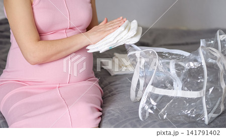 Pregnant woman packing baby diapers for hospital bag Pregnant woman packing baby diapers for hospital bag 141791402