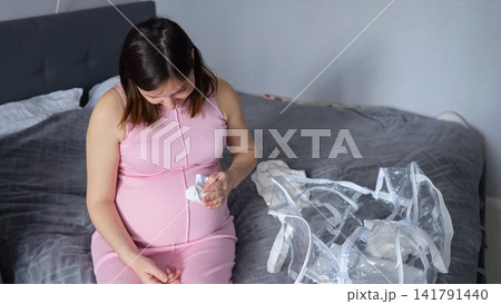 Pregnant woman preparing baby clothes for hospital bag Pregnant woman preparing baby clothes for hospital bag 141791440