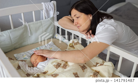 Mother gently caressing sleeping newborn baby in crib Mother gently caressing sleeping newborn baby in crib 141791487