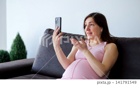Pregnant woman having video call on smartphone at home Pregnant woman having video call on smartphone at home 141791549