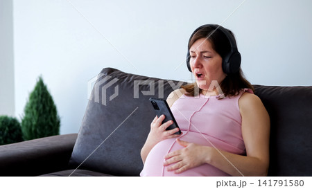 Pregnant woman feeling tired yawning while using smartphone Pregnant woman feeling tired yawning while using smartphone 141791580
