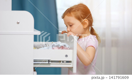 Curious little girl exploring clothes in open dresser drawer Curious little girl exploring clothes in open dresser drawer 141791609