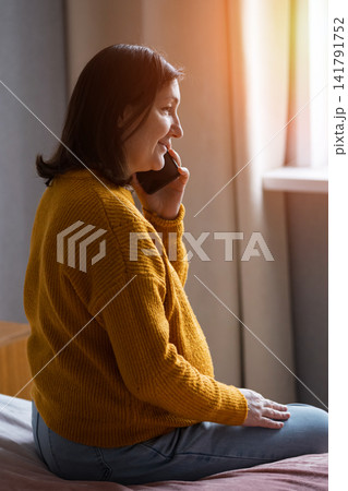 Pregnant woman in yellow sweater sitting indoors by a window in soft morning light Pregnant woman in yellow sweater sitting indoors by a window in soft morning light 141791752
