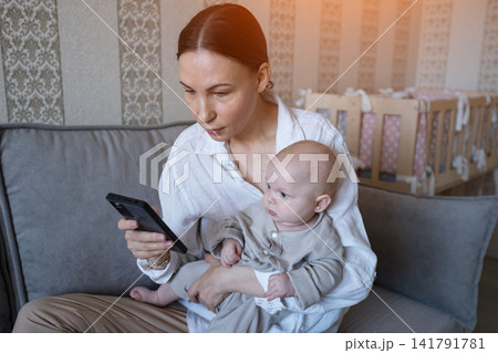 Young mother holding baby and using smartphone Young mother holding baby and using smartphone 141791781
