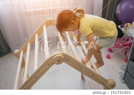 Toddler child playing on climbing wooden pikler triangle Toddler child playing on climbing wooden pikler triangle 141791803