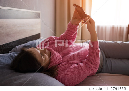 Pregnant woman in cozy knit dress stretching on bed at home with warm morning sunlight Pregnant woman in cozy knit dress stretching on bed at home with warm morning sunlight 141791826