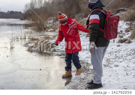 Two boys with school backpacks walk on thin dangerous ice on a frozen river Two boys with school backpacks walk on thin dangerous ice on a frozen river 141792059