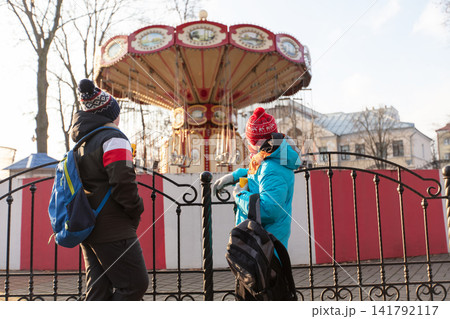 Two schoolchildren with backpacks look at a colorful carousel in the park Two schoolchildren with backpacks look at a colorful carousel in the park 141792117
