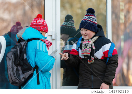 Kids chatting and playing outside a school during winter while wearing colorful hats and jackets Kids chatting and playing outside a school during winter while wearing colorful hats and jackets 141792119