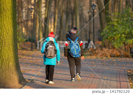 Children walk on a path in a park surrounded by trees during the afternoon in autumn weather Children walk on a path in a park surrounded by trees during the afternoon in autumn weather 141792120