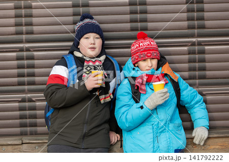 Two school age children in winter clothes drinking hot drinks outdoors Two school age children in winter clothes drinking hot drinks outdoors 141792222