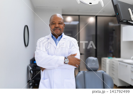 Confident black male dentist standing with folded arms in modern dentistry clinic Confident black male dentist standing with folded arms in modern dentistry clinic 141792499