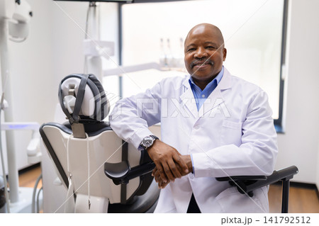 Experienced black male dentist leaning on dental chair in bright clinic Experienced black male dentist leaning on dental chair in bright clinic 141792512