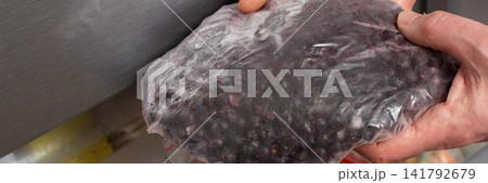 A man is taking a bag of frozen currants out of the refrigerator. He may be getting ready to use the fruits in a recipe. The scene is set in a kitchen, with various items in the freezer, banner 141792679