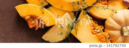 Pumpkin slices are arranged on a kitchen counter with fresh herbs nearby. The scene shows the preparation of seasonal dishes in the fall, banner Pumpkin slices are arranged on a kitchen counter with fresh herbs nearby. The scene shows the preparation of seasonal dishes in the fall, banner 141792730