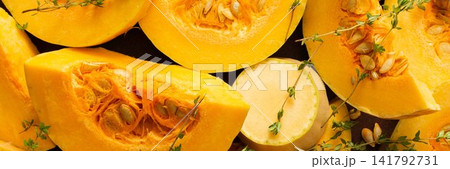 Slices of yellow squash are laid out on a wooden surface. Fresh thyme sprigs are placed on the squash. This scene shows preparation for cooking a meal or dish, banner 141792731