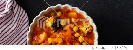 A bowl holds bright red soup made with vegetables like tomatoes, carrots, potatoes, and broccoli, served alongside gluten-free flaxseed bread for a healthy meal, banner A bowl holds bright red soup made with vegetables like tomatoes, carrots, potatoes, and broccoli, served alongside gluten-free flaxseed bread for a healthy meal, banner 141792763