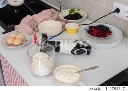 A person is mixing butter and flour with a blender while preparing to make a strawberry, currant, and blueberry shortbread pie with a sour cream sauce in a kitchen setting A person is mixing butter and flour with a blender while preparing to make a strawberry, currant, and blueberry shortbread pie with a sour cream sauce in a kitchen setting 141792847