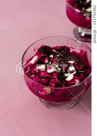 Two bowls of healthy ice cream sit on a table. The ice cream features strawberries, bananas, beets, and Greek yogurt. Chocolate and nuts top the creamy dessert. Spoons are beside the bowls Two bowls of healthy ice cream sit on a table. The ice cream features strawberries, bananas, beets, and Greek yogurt. Chocolate and nuts top the creamy dessert. Spoons are beside the bowls 141792862