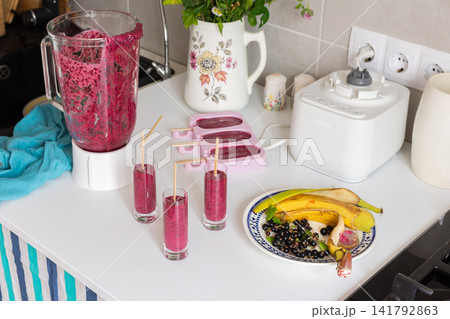 Currant banana homemade ice cream is made on a kitchen counter. A blender is used to mix the ingredients. Small glasses and popsicle molds are on the table Currant banana homemade ice cream is made on a kitchen counter. A blender is used to mix the ingredients. Small glasses and popsicle molds are on the table 141792863