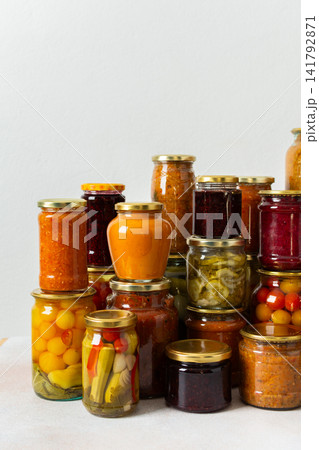 Canned vegetables and fruits are stacked on a shelf, prepared for winter use. Various jars hold different preserves, showcasing careful efforts for storing food during the season 141792871