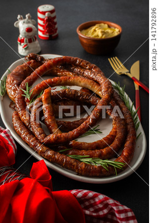 A Christmas table is set with fried pork sausage in the center. Red flowers and festive decorations surround the food as families gather to celebrate during the evening 141792896