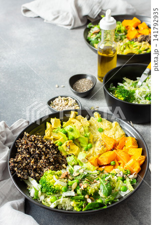 A quinoa bowl is arranged with roasted pumpkin, hummus, and a fresh salad. Plates are set on a table with utensils. Sunshine comes through the window A quinoa bowl is arranged with roasted pumpkin, hummus, and a fresh salad. Plates are set on a table with utensils. Sunshine comes through the window 141792935