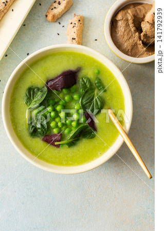 A bowl of creamy broccoli and green pea soup sits on a green plate. Next to it is liver pate in a small dish and grissini on a white platter. This meal provides healthy options A bowl of creamy broccoli and green pea soup sits on a green plate. Next to it is liver pate in a small dish and grissini on a white platter. This meal provides healthy options 141792939