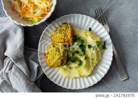 This plate features mashed potatoes, two turkey meatballs, and a side of fermented cabbage. Fresh herbs are sprinkled on top, creating a balanced meal choice 141792970