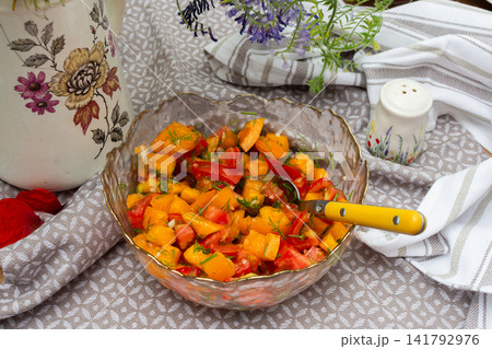 A bowl of salad contains yellow and red tomatoes along with garlic and dill. The bowl is placed on a patterned cloth with simple kitchen items nearby A bowl of salad contains yellow and red tomatoes along with garlic and dill. The bowl is placed on a patterned cloth with simple kitchen items nearby 141792976