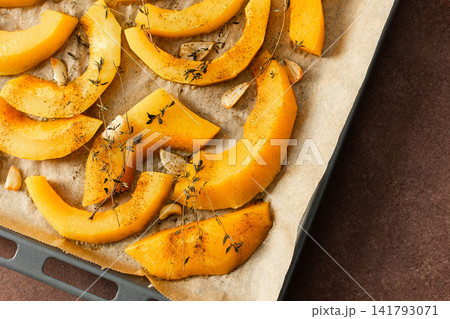 Butternut squash slices are arranged on a tray with herbs and garlic, ready for roasting. This is part of a cooking process in a kitchen setting Butternut squash slices are arranged on a tray with herbs and garlic, ready for roasting. This is part of a cooking process in a kitchen setting 141793071
