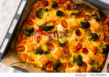 Salmon is baked along with broccoli, tomatoes, and eggs on a deck. This meal is set up for a healthy breakfast or lunch. The food looks fresh and ready to eat 141793094