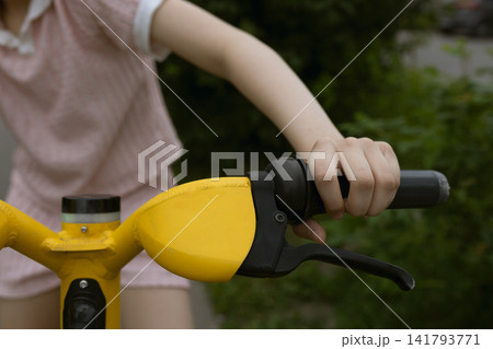 Close up view of kid's hand gripping the handle of bright yellow bike or scooter, enjoying active outdoor recreation and fitness lifestyle in park during summer Close up view of kid's hand gripping the handle of bright yellow bike or scooter, enjoying active outdoor recreation and fitness lifestyle in park during summer 141793771