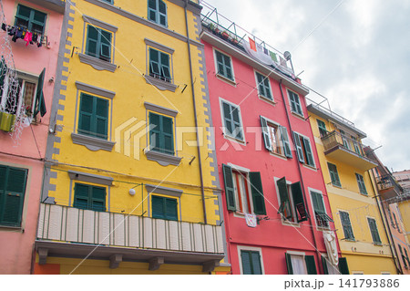 Low angle view of vibrant yellow, pink residential building facades with green shutters in village of Cinque Terre National Park. Traditional Mediterranean coastal town in Liguria, Italy Low angle view of vibrant yellow, pink residential building facades with green shutters in village of Cinque Terre National Park. Traditional Mediterranean coastal town in Liguria, Italy 141793886
