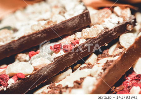 Artisan handmade dark chocolate bars with assorted nuts dried fruits and sugar crystals close-up Artisan handmade dark chocolate bars with assorted nuts dried fruits and sugar crystals close-up 141793943