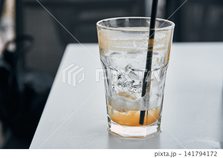 Close-up of a nearly empty iced beverage glass with a black straw on a white table Close-up of a nearly empty iced beverage glass with a black straw on a white table 141794172