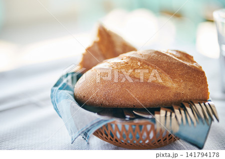 Fresh crusty bread loaf served in a small basket with cutlery on dining table 141794178