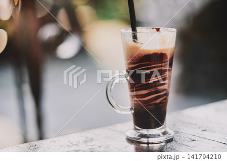 Close-up of a refreshing iced chocolate drink served in a tall glass with a straw 141794210