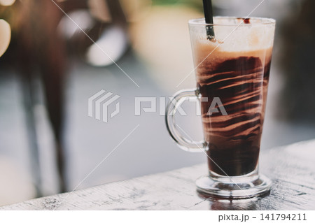 Close-up of a refreshing iced coffee beverage in a tall glass mug on a wooden table Close-up of a refreshing iced coffee beverage in a tall glass mug on a wooden table 141794211
