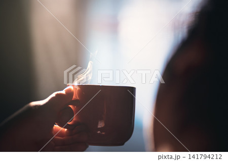 Close-up of a person holding a steaming ceramic cup of hot coffee indoors 141794212