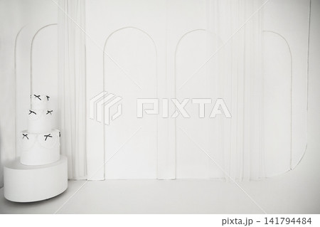 Elegant white three-tiered cake with black bows in minimalist arch interior Elegant white three-tiered cake with black bows in minimalist arch interior 141794484