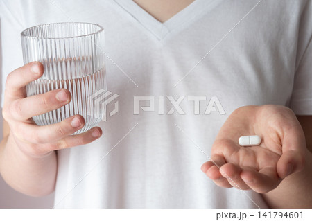 Girl in white clothes take the pill and glass with water in the hand. Healthcare from pharmacy. Kid sit at home because of illness. 141794601