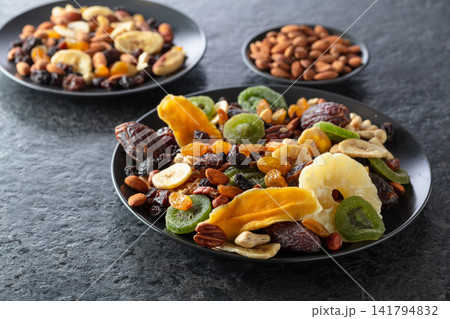 Dried tropical fruits, nuts, and raisins in black plate. Dried tropical fruits, nuts, and raisins in black plate. 141794832