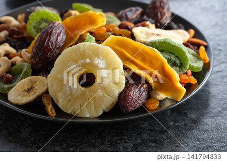 Dried tropical fruits, nuts, and raisins in black plate. Dried tropical fruits, nuts, and raisins in black plate. 141794833