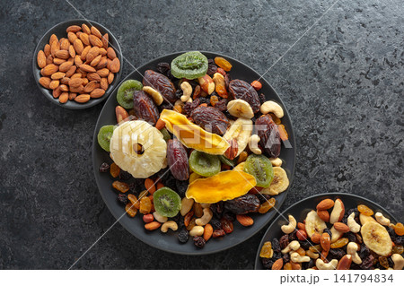 Dried tropical fruits, nuts, and raisins in black plate. Dried tropical fruits, nuts, and raisins in black plate. 141794834