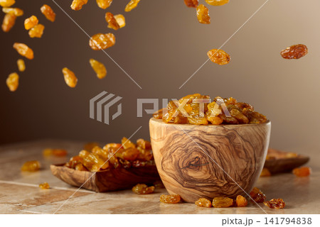 Yellow sultana raisins pour into a wooden bowl. Yellow sultana raisins pour into a wooden bowl. 141794838