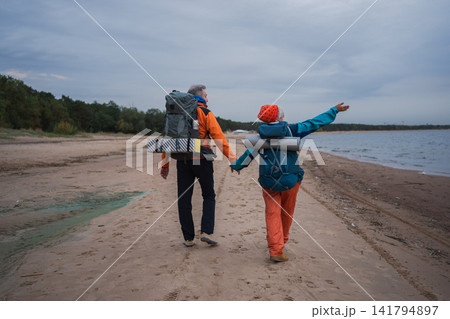 Hiking tourism adventure. Senior couple man woman enjoying outdoor recreation hiking on beach. Happy old people backpackers hikers enjoy walking hike trekking tourism active vacation beauty of nature Hiking tourism adventure. Senior couple man woman enjoying outdoor recreation hiking on beach. Happy old people backpackers hikers enjoy walking hike trekking tourism active vacation beauty of nature 141794897