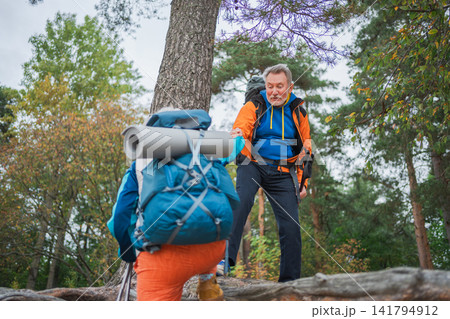 Hiking adventure. Man helping hand woman on hiking in forest. Senior couple enjoying outdoor recreation hiking. Happy old people backpackers hikers enjoy walking hike trekking tourism active vacation Hiking adventure. Man helping hand woman on hiking in forest. Senior couple enjoying outdoor recreation hiking. Happy old people backpackers hikers enjoy walking hike trekking tourism active vacation 141794912